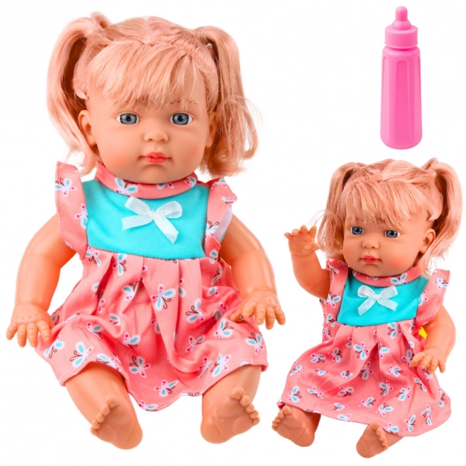 Puppenbaby im bunten Kleid mit Flasche und Geräuschen